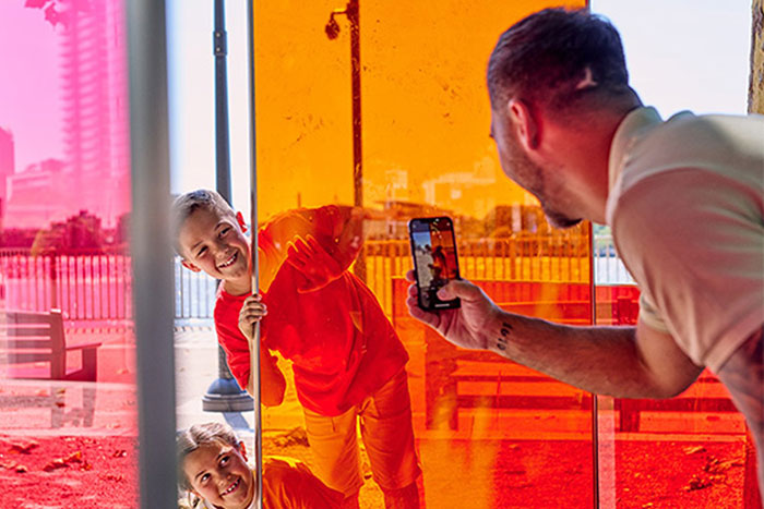 A father photographing a child standing in front of a vibrant glass wall